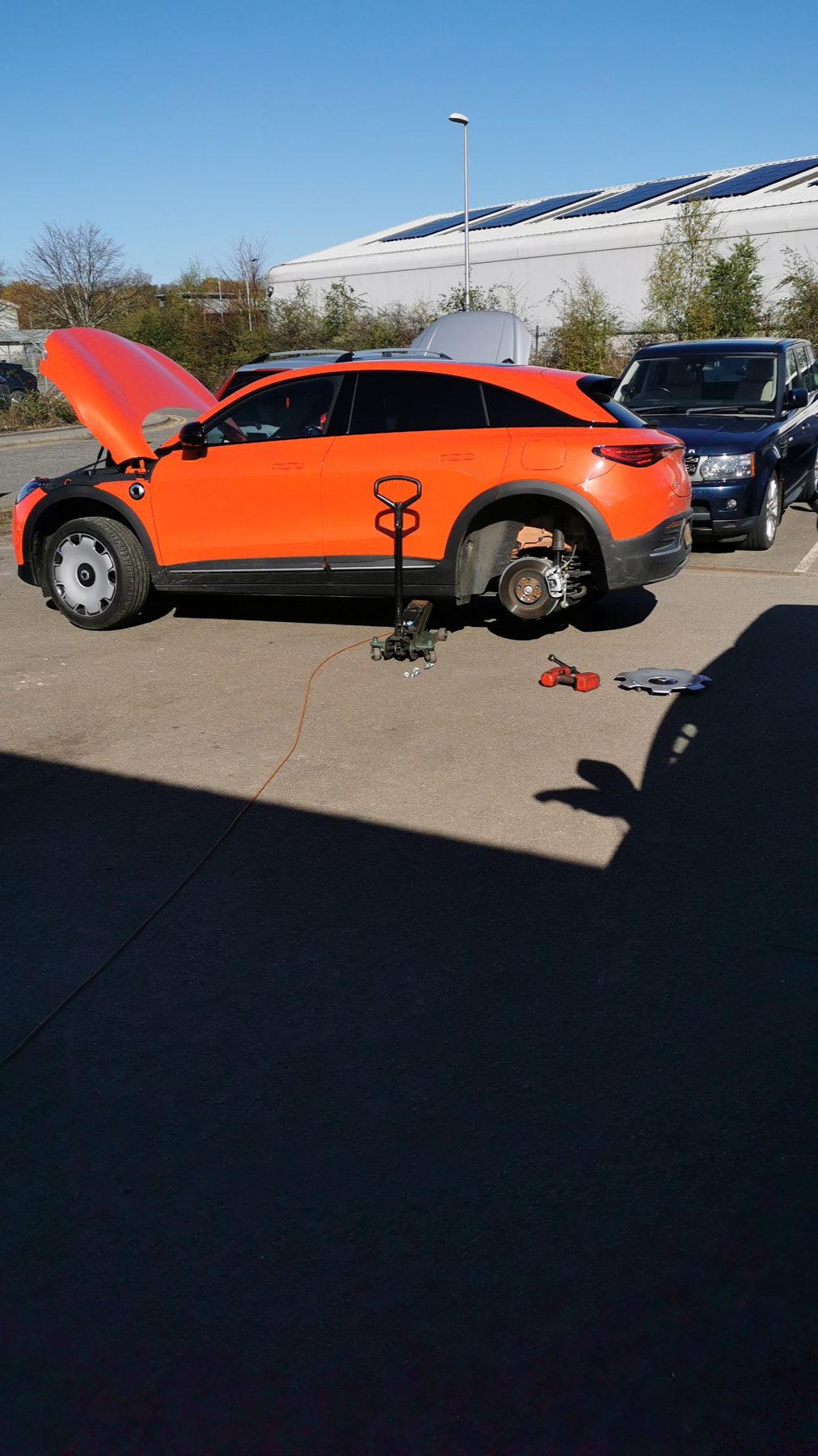 An orange car with a wheel off in the yard