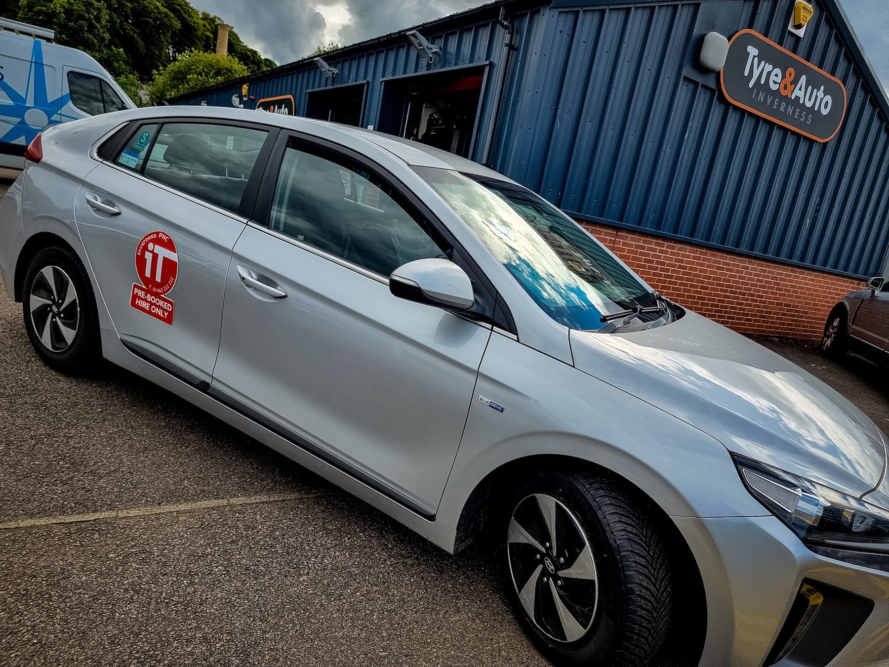 A silver hatchback outside the workshop under the Tyre&Auto sign