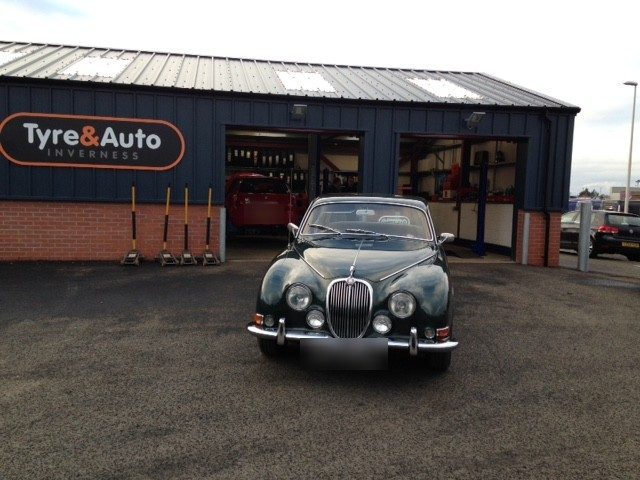 A classic Jaguar parked in front of the Tyre&Auto workshop